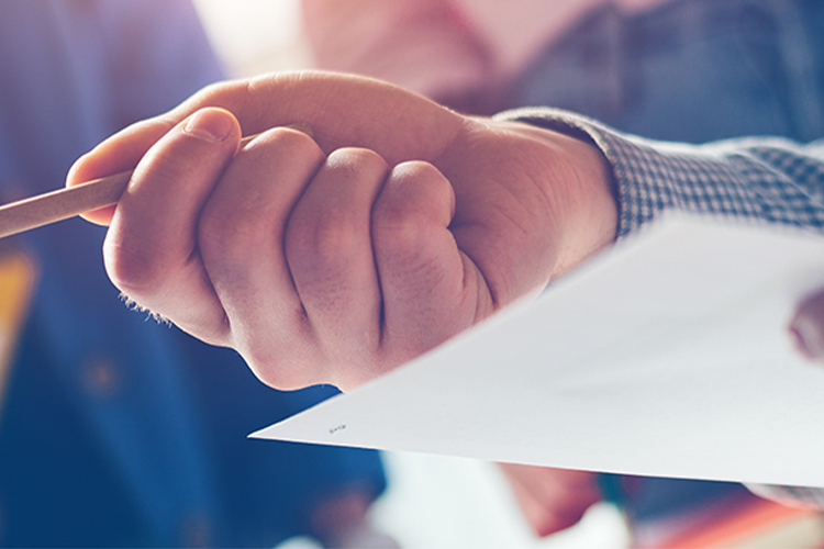 Close-up of two people’s hands; one holds a pencil and points, the other holds a piece of paper, suggesting discussion or collaboration.